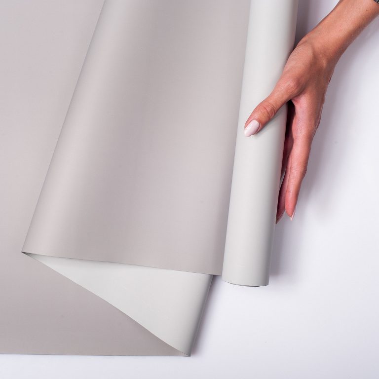 A closeup of a woman holding a roll of gray wallpaper against a white background